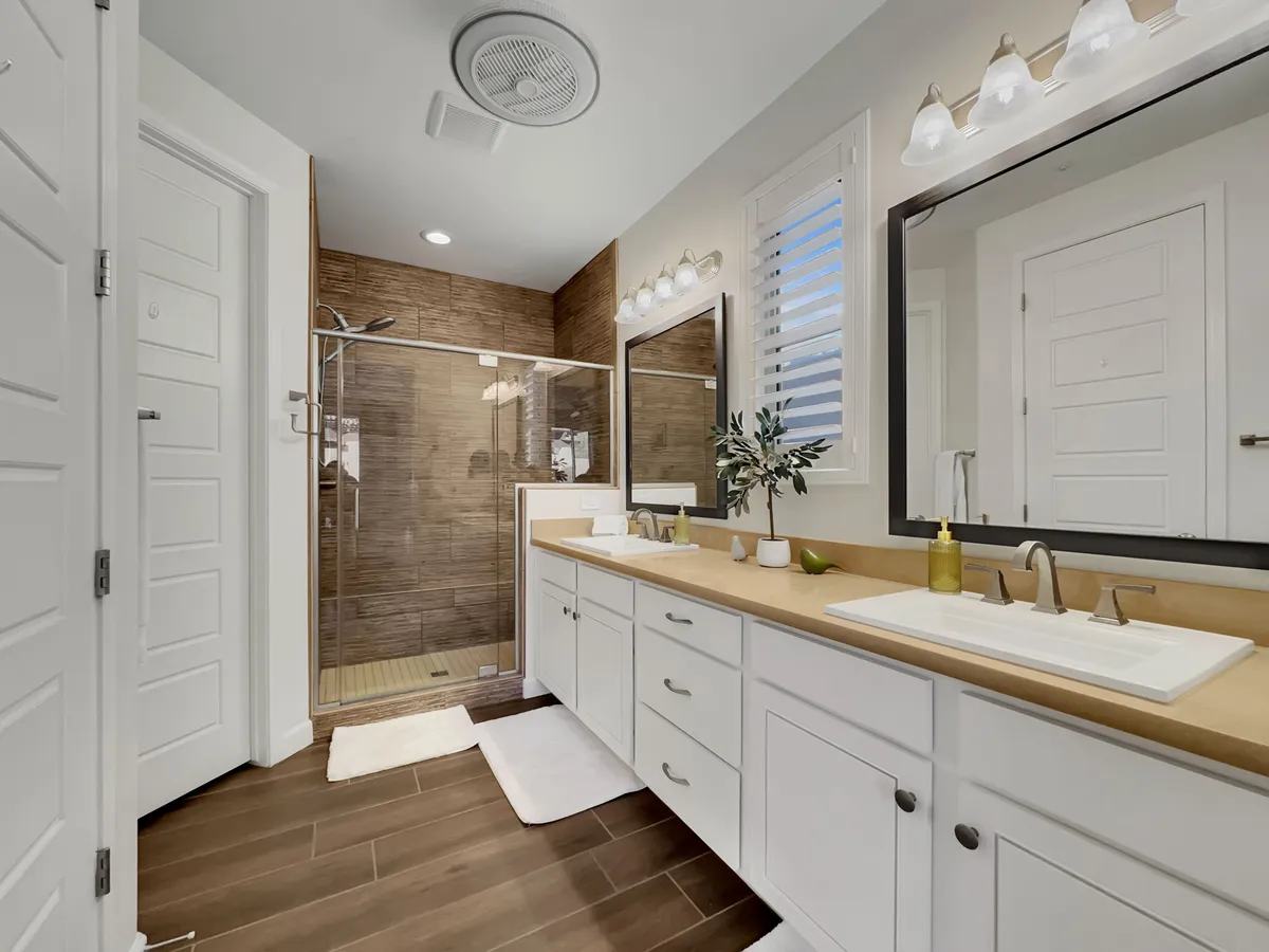 A modern bathroom featuring a double vanity with sleek sinks, a glass shower enclosure, large mirrors, and a touch of greenery for relaxation. The space feels fresh and spa-inspired, inviting guests to unwind with self-care rituals or start the day feeling rejuvenated.