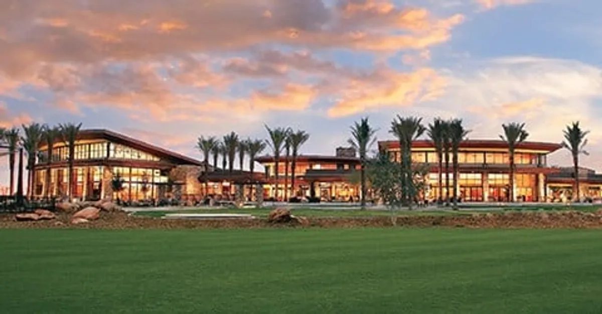 A striking exterior scene featuring large glass windows framed by lush palm trees and modern architecture. In the foreground, people are gathered outdoors, relaxing in the garden as the sun sets, creating a warm, welcoming atmosphere ideal for social events and community gatherings.