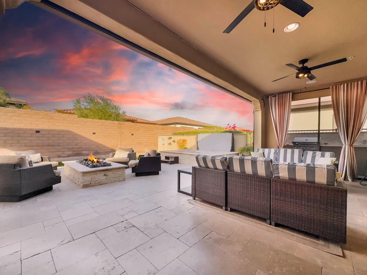An inviting outdoor fire pit area surrounded by cozy seating and draped curtains, set against a sky painted with sunset colors. The arrangement is perfect for evening gatherings and relaxation, with the warm glow of the firepit creating a serene and intimate atmosphere.