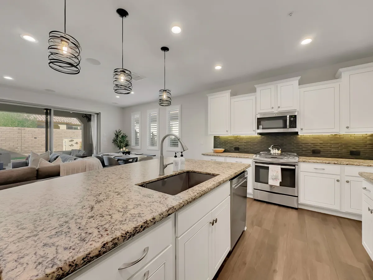 A contemporary kitchen with granite countertops and stainless steel appliances. Pendant lighting hangs above the workspace, and the open layout seamlessly connects the kitchen to the living area, suggesting a social environment for entertaining guests or enjoying family time.