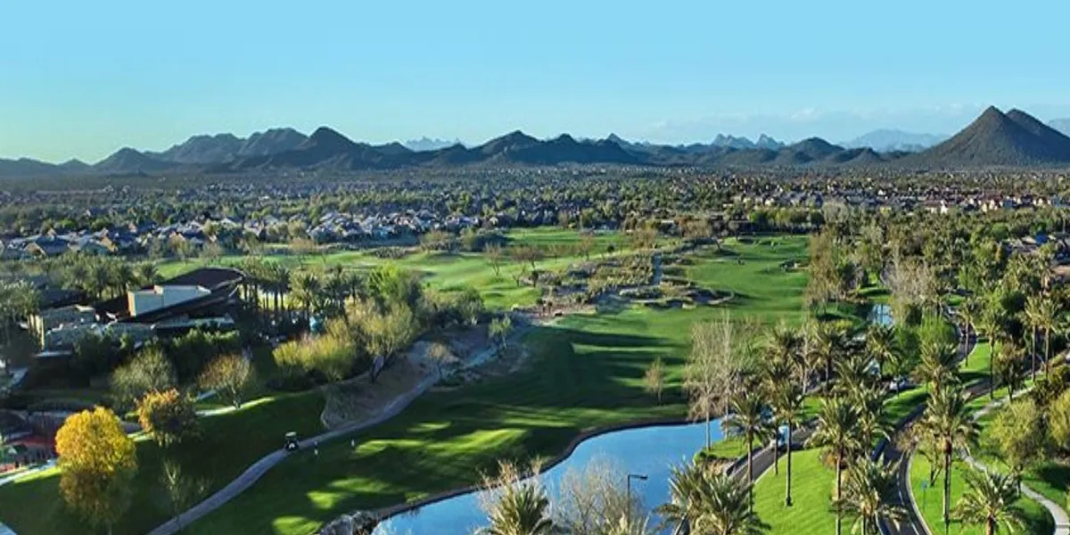 A panoramic view of a lush golf course with palm trees, mountains, and water features stretching out beneath a vibrant sky. The scene suggests both relaxation and activity, hinting at community events, nature walks, and the appealing local landscape.