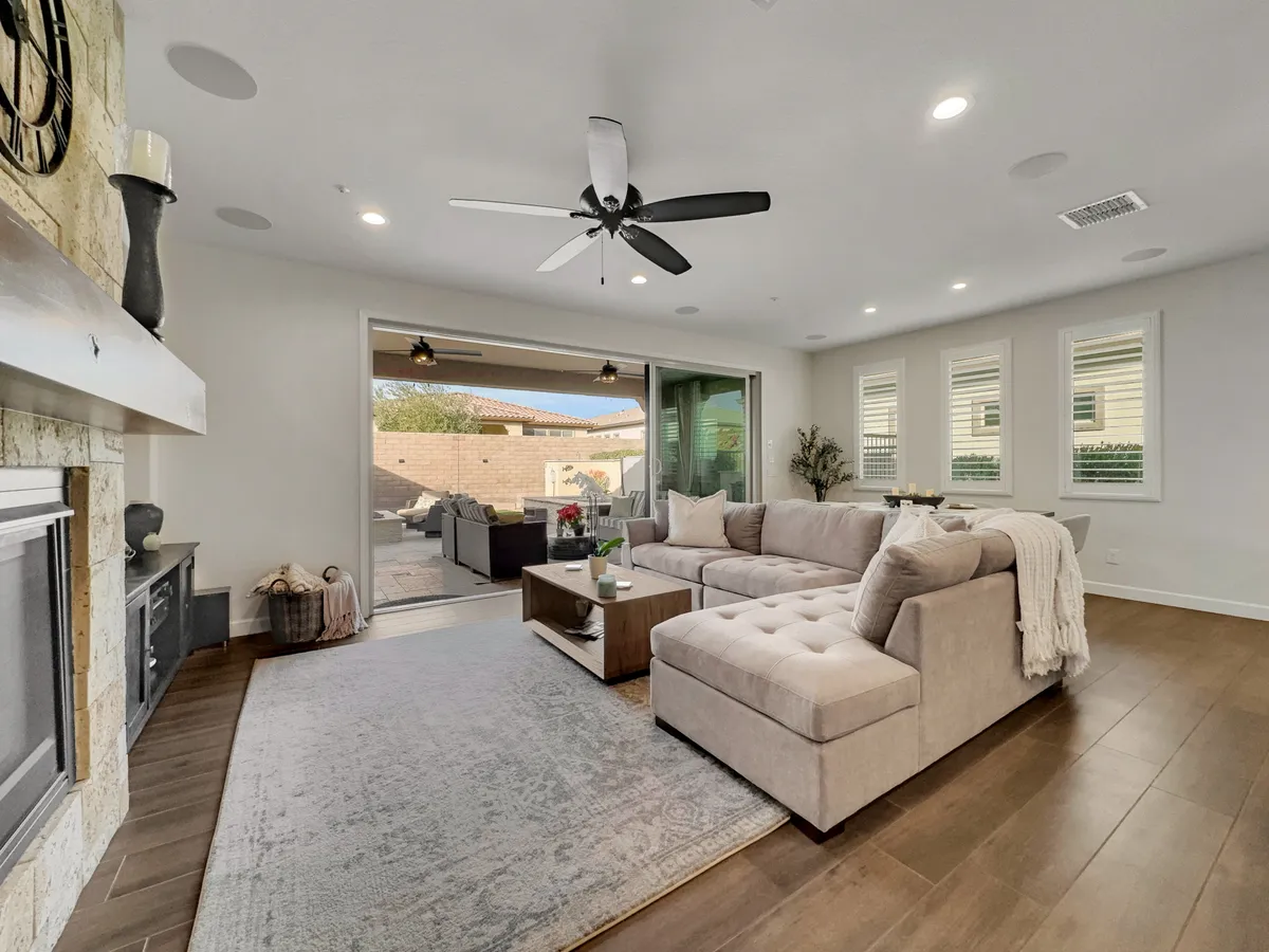 A cozy living room with a sectional sofa, coffee table, fireplace, and a large sliding glass door that connects the interior space to the outdoors. Sunlight streams in, hinting at the inviting patio or garden area just beyond the glass.